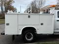 A white 2013 RAM 3500 truck with a service body featuring multiple storage compartments and a mounted ladder rack on top
