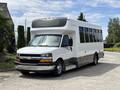 A 2020 Chevrolet Express shuttle bus with a white exterior and large tinted windows parked at an angle showcasing its front and side design