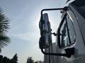 A 2010 Freightliner M2 106 truck with a shiny side mirror and a prominent door, reflecting the sunlight