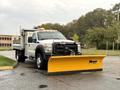 A 2013 Ford F-450 Super Duty truck with a yellow snowplow attached to the front and a flatbed in the rear