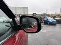 A close-up of the side mirror of a red 2016 Mitsubishi Outlander showing a blurred background of vehicles and rain droplets on the mirror