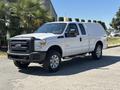 A white 2014 Ford F-250 Super Duty pickup truck with a truck cap and chrome wheels parked on a road