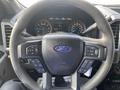 Steering wheel of a 2016 Ford F-150 featuring controls and a Ford logo in the center with a digital dashboard displayed behind it