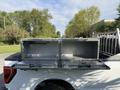 A white 2021 Ford F-150 with a silver diamond plate truck bed tool box featuring two open compartments on its rear