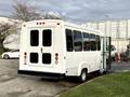 A 2002 Ford Econoline bus with a white exterior and large rear doors parked on a lot