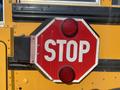 A red octagonal stop sign with white letters mounted on the side of a yellow school bus
