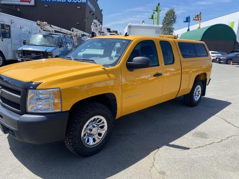 A bright yellow 2012 Chevrolet Silverado 1500 pickup truck with a covered bed and chrome wheels parked on a pavement