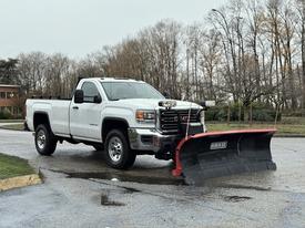 A white 2017 GMC Sierra 3500HD with a red snow plow attachment in the foreground