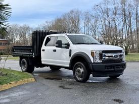 A 2017 Ford F-450 Super Duty truck with a white cab and black flatbed parked on a road
