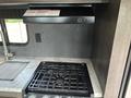 A modern kitchen stove with a black gas grill top and a gray countertop featuring a sink and a range hood above it