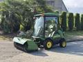 A 2021 John Deere 1575 lawn mower with a cab and a large brush attachment in the front parked on a path