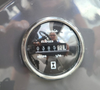 A circular hour meter displaying 038591 hours with a reflective surface showing a person’s outline in the background