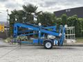 A blue 2016 Genie TZ-34/20 boom lift with extended arms and a basket for workers on a trailer with wheels