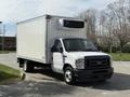 A 2023 Ford E-450 truck with a cargo box and a refrigeration unit on top parked in an outdoor area