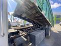 A 1997 Freightliner FL70 truck with a raised green dump bed revealing the hydraulic lift mechanism and undercarriage details