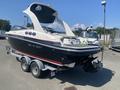 A 2013 Larson 238 boat with a sleek design featuring a dark hull, white accents, and a raised motorized canopy is mounted on a dual-axle trailer