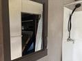A bathroom mirror reflects an interior view of a 2021 Jayco Jay Flight trailer showing a showerhead and part of a bed in the background