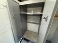 A gray storage cabinet with double doors open revealing two shelves and a bare interior without items