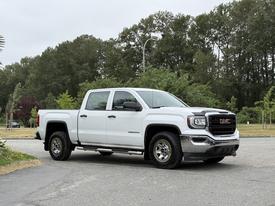 A 2016 GMC Sierra 1500 pickup truck in white with chrome accents parked, featuring four doors and large wheels