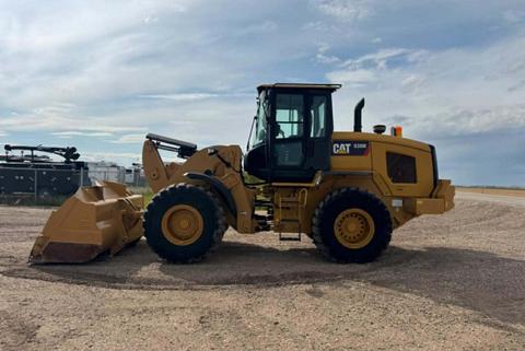 A 2016 CAT 938M wheel loader with a yellow body and large front bucket is positioned on gravel. The cabin features a large glass panel for visibility and the company logo is visible on the side