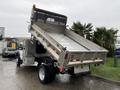A 2015 Ford F-450 dump truck with its bed raised, showcasing a metal bed and a rear-mounted hydraulic system