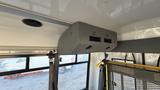The image shows a gray overhead air conditioning unit installed in a vehicle with vents facing downwards