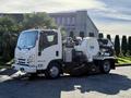 A 2016 Isuzu NPR with a large suction and sweeping attachment mounted on its chassis parked on a paved surface