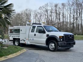 A 2008 Ford F-450 truck in white with a flatbed and utility box attached on the side