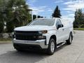 A white 2019 Chevrolet Silverado 1500 with a glossy finish and chrome accents parked on a driveway with a truck cap on the bed and running boards along the sides