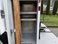 An open compartment of a 2005 Freightliner M2 106 with metal shelves inside and a wooden board covering part of the entrance
