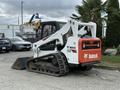 A 2017 Bobcat T740 compact track loader with a front bucket and rubber tracks is parked on a surface with various vehicles and machinery in the background