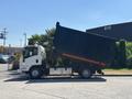 A 2016 Isuzu NPR-HD truck with a raised black dumpster attached at the back in a side view position
