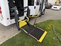 A wheelchair lift is extended from the back of a 2013 Chevrolet Express, featuring a black mesh platform with yellow safety features and straps for securing mobility devices