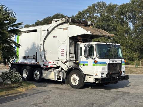 A 2011 Autocar Xpeditor garbage truck with a white body and green and blue stripes on the side is parked on a street