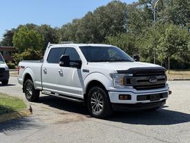 A white 2018 Ford F-150 pickup truck with black accents and large wheels parked on a driveway