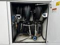 A compartment containing hoses on reels along with a black tank and various fittings and valves inside a service vehicle