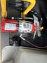 A red fire extinguisher mounted on a floor with a label displaying instructions and a metal handle near various wires and a switch