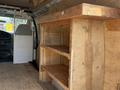 A 2008 Ford Econoline van interior featuring a wooden shelving unit with two open shelves and a partitioned area behind the driver's seat