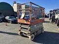 A 2010 SkyJack SJ scissor lift with a rusty red frame and yellow hazard stripes on the base