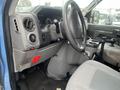 Interior view of a 2009 Ford Econoline with a steering wheel control panel and gear shifter visible along with light gray seats and cup holders