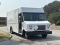 A white 2018 Ford Econoline delivery truck with an open door and a flat front design parked on a gravel surface