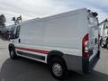 A 2017 RAM Promaster van with a white body and a red strip along the side parked at an industrial location