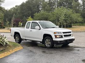 A white 2011 Chevrolet Colorado pickup truck with a short bed and two doors parked on a slight incline