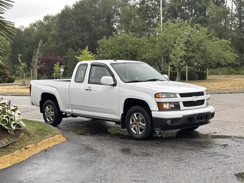 A white 2011 Chevrolet Colorado pickup truck with a short bed and two doors parked on a slight incline