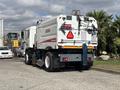 A 2012 Autocar Xpert street sweeper with a white and red color scheme featuring a broom attachment and a caution sign on the back