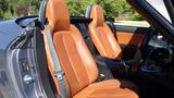 Interior of a 2007 Mazda Miata featuring two orange leather seats with seatbelts and a black console between them