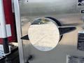 A shiny circular fuel cap with a black lever handle attached to a Freightliner FL80 truck's side panel