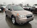 A 2016 Subaru Forester in a light bronze color parked with rain on the surface reflecting the vehicle's contours and details