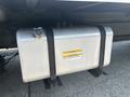 A silver fuel tank mounted underneath a 2012 Hino 338 truck secured with black straps and featuring a yellow label with safety and capacity information