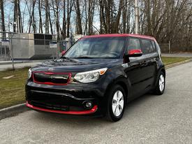 A black 2016 Kia Soul EV with a red roof and trim parked on a paved area showcasing its unique boxy shape and modern design
